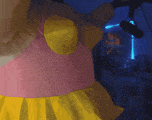 a woman in a pink and yellow dress stands in front of a microphone in a dark room