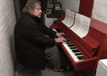a man is playing a red piano with sheet music on top
