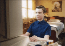 a young boy in a blue shirt is typing on a computer keyboard