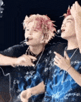 a couple of people standing next to each other on a stage . one of the people has pink hair .