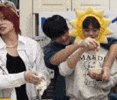 a group of people are standing next to each other in a kitchen . one of the people is wearing a yellow sun hat .