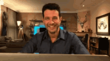 a man is smiling while sitting in front of a laptop in a living room
