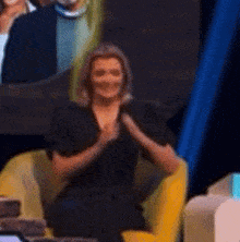 a woman in a black dress is sitting in a yellow chair with her hands covering her mouth