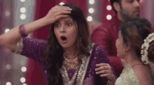 a woman in a purple dress is holding her hand to her forehead and making a surprised face .