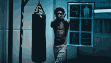 a shirtless man stands in front of a boxing bag