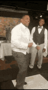 a man in a tuxedo is dancing on a dance floor with two waiters behind him .