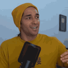 a man wearing a yellow shirt and a yellow beanie is smiling in front of a microphone