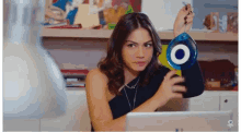 a woman in a black one shoulder top is holding a blue evil eye