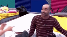 a man in a striped shirt is sitting on a bed and laughing