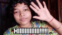 a woman in a green shirt waves her hand in front of a sign that says " hi "