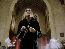 a man in a black coat is holding a chain and a cross
