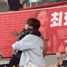 a man is hugging another man in front of a large red sign that says ' a ' on it .