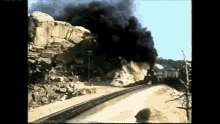 a train is going down the tracks with smoke coming out of the rocks