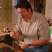 a man in a striped shirt says hot damn while holding a piece of food
