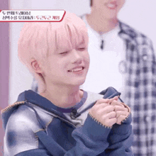 a young man with pink hair is smiling with his eyes closed and his hands folded .