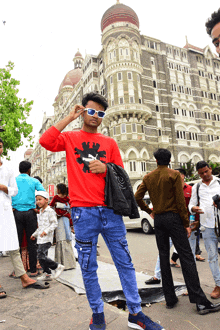 a man wearing sunglasses stands in front of a building that says ' the taj mahal ' on it