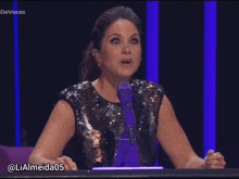 a woman sitting at a table with a purple microphone and the name lialmeida05 on the bottom right