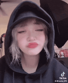 a girl wearing a black hoodie and a hat has a tiktok sticker on her shirt