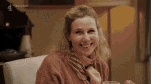 a woman in a pink sweater and scarf smiles while sitting in a chair with the words stay at home below her