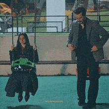 a man in a suit stands next to a woman on a swing with minimalmoons written on the bottom right