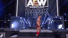 a wrestler is standing in front of a aew wrestling dark elevation sign