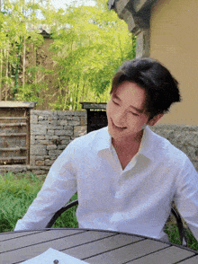 a man in a white shirt is smiling while sitting at a table outside