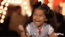 a little girl is laughing with her fist in the air and saying yay .