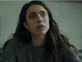 a woman wearing a grey sweater and earrings looks surprised