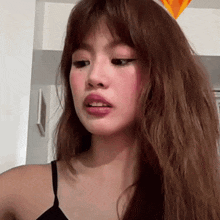 a woman with long hair and pink lips is wearing a black tank top and making a funny face .