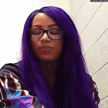 a woman with purple hair and glasses is standing in front of a white wall .