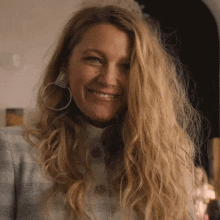 a woman wearing hoop earrings and a plaid jacket is smiling