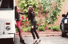 two women are standing next to each other in front of a truck .