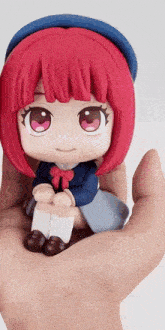 a person is holding a figurine of a girl with red hair and a blue hat