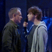 a man is holding a microphone and talking to a young man