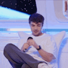 a man is sitting on a couch holding a microphone and looking at his phone .