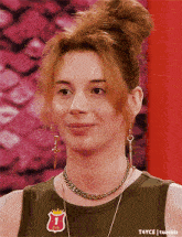 a woman wearing earrings and a necklace has a patch on her shirt that says 1
