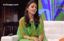 a woman in a green dress is sitting on a couch smiling .