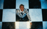 a man in a striped shirt and tie stands on a black and white checkered floor