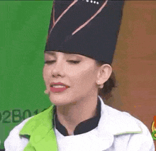 a woman wearing a chef 's hat and a green jacket is talking on a microphone .