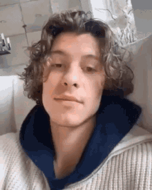 a young man with curly hair is sitting on a couch and looking at the camera .
