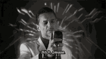a man in a white suit is holding a cell phone and says " bitch please "