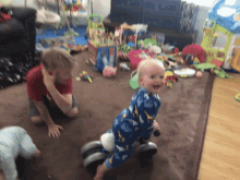 a baby is riding a toy bike in a living room while a boy looks on