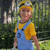 a young boy in a minion costume is standing in front of a metal fence .