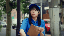 a woman wearing a blue hat and a blue shirt is holding a piece of paper