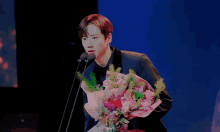 a man in a suit is holding a bouquet of flowers and speaking into a microphone