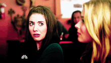 two women are sitting next to each other and one of them is making a surprised face .