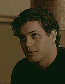 a man with curly hair is wearing a black shirt and looking at the camera .