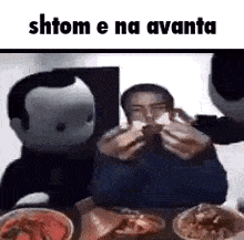a man is sitting at a table eating a sandwich while a stuffed animal looks on .
