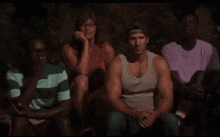a group of people are sitting in a circle with one man wearing a tank top