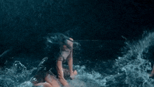 a woman in a bikini is kneeling in the water with water splashing around her